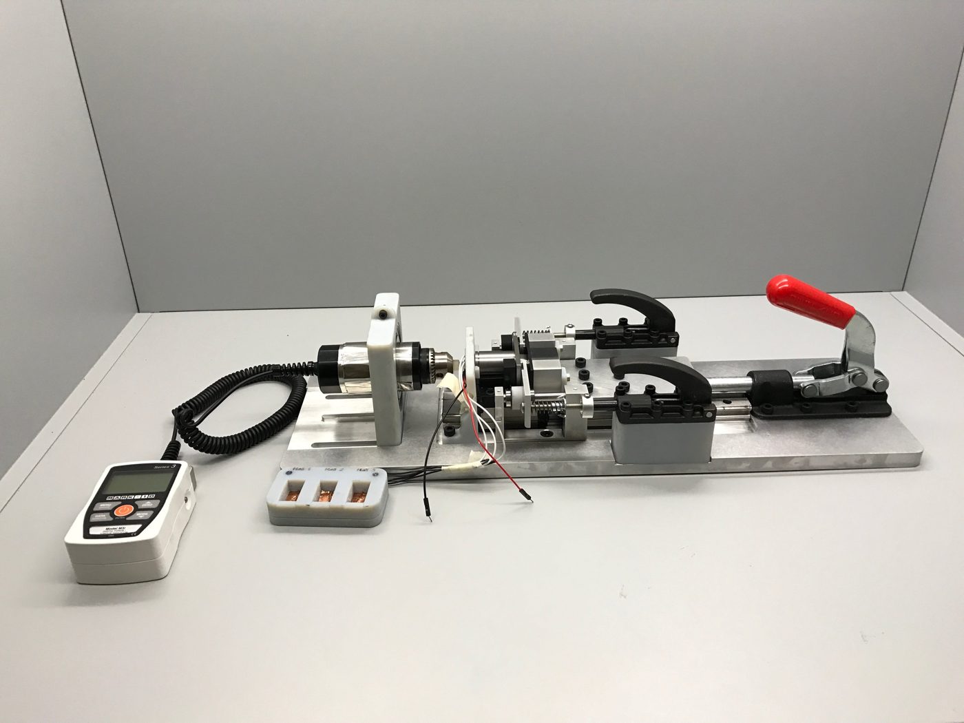 Bolt test fixture on an aluminum plate with toggle clamps, a linear slide and a Mark-10 gauge beside it